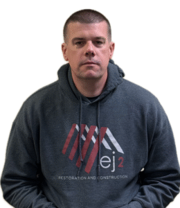 Portrait of a man in a dark gray hoodie with a red/white graphic and the words 'Restoration and Construction' on the chest, looking at the camera.