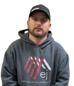 Portrait of a man facing the camera, wearing a dark gray hoodie with a red and white logo and a black Behr cap.