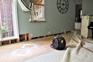 Living room under renovation with exposed subfloor, cords on the wall, and a large wall clock. A windowed door is on the left.